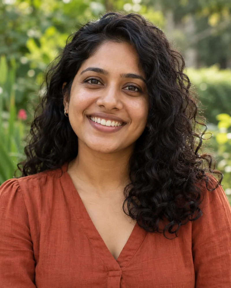 Illustrative portrait of a smiling South Asian woman in a rust blouse in a garden