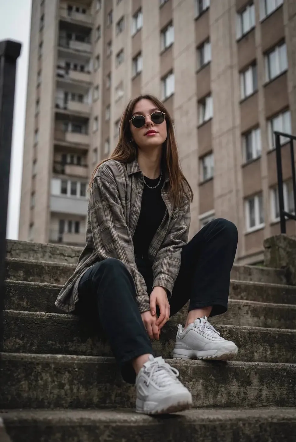 { "subject": "Young woman sitting casually on outdoor concrete stairs, posing…