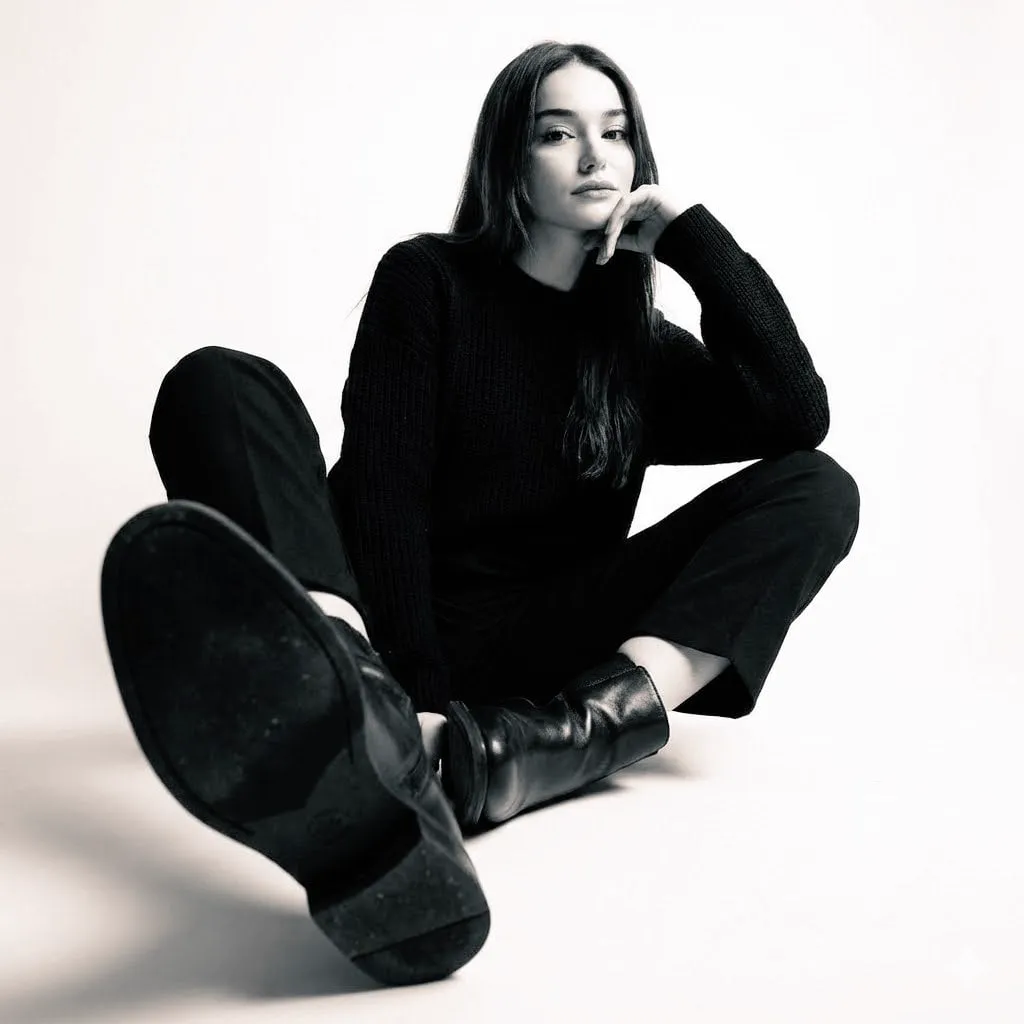 High-contrast black-and-white studio photo of a woman seated on the floor…