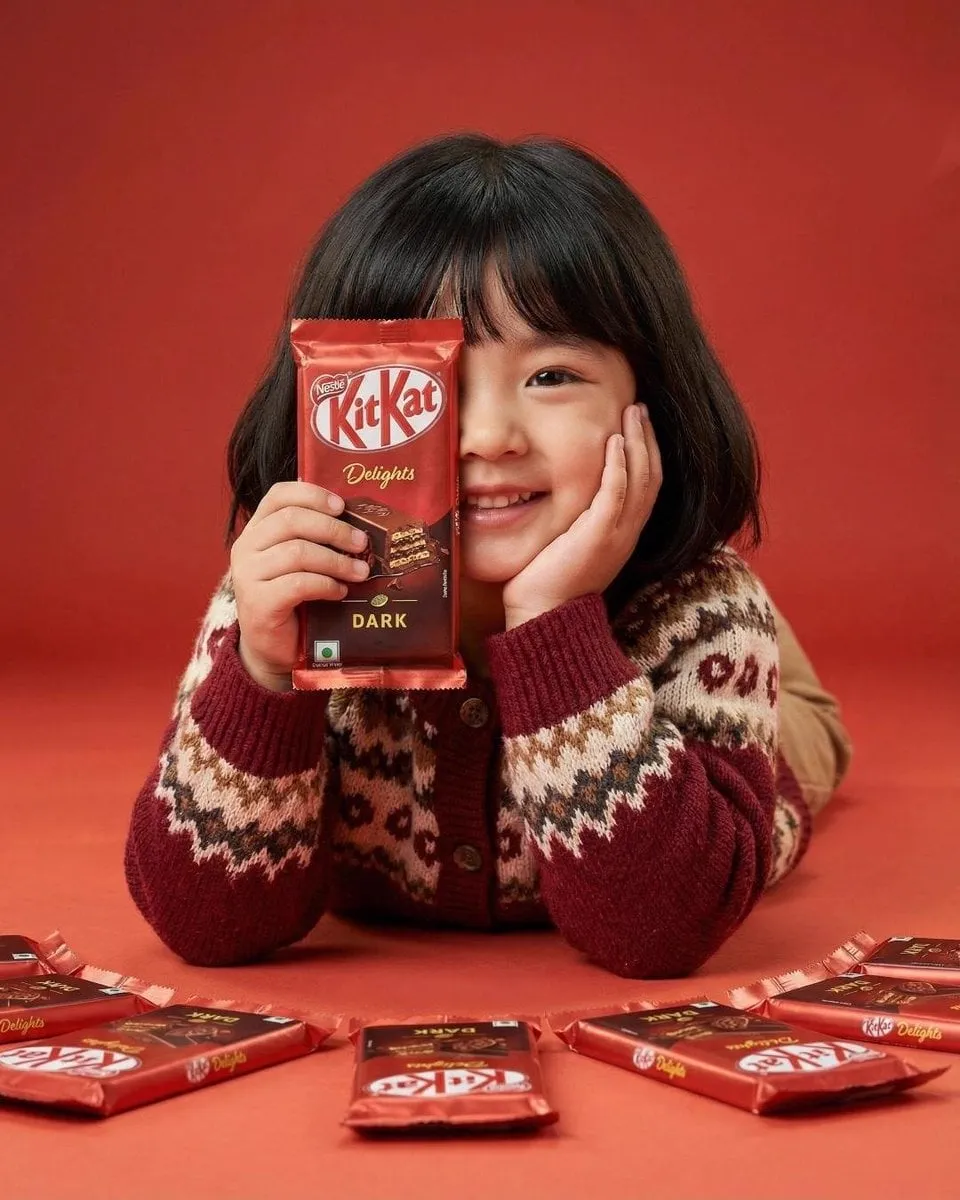 A cute young girl with short black hair and bangs smiling while holding a red…